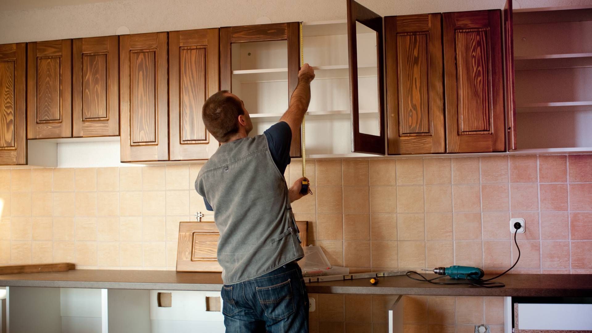 A man is measuring a cabinet in a kitchen with a tape measure.