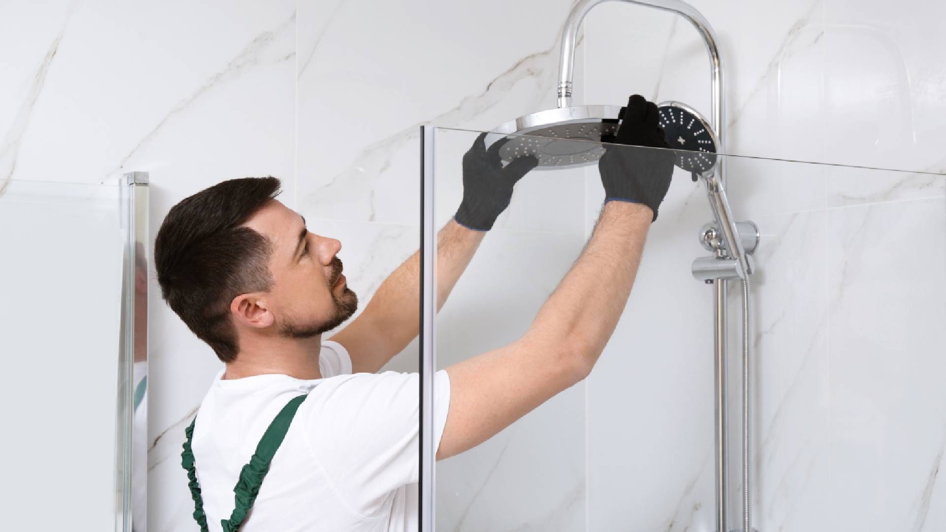 A man is installing a shower head in a bathroom.