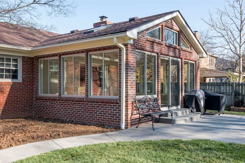 A brick house with a large sunroom and a bench in front of it.