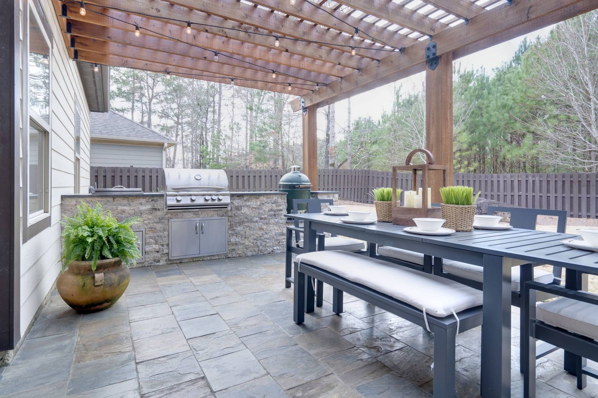 A patio with a table and benches and a grill under a pergola.