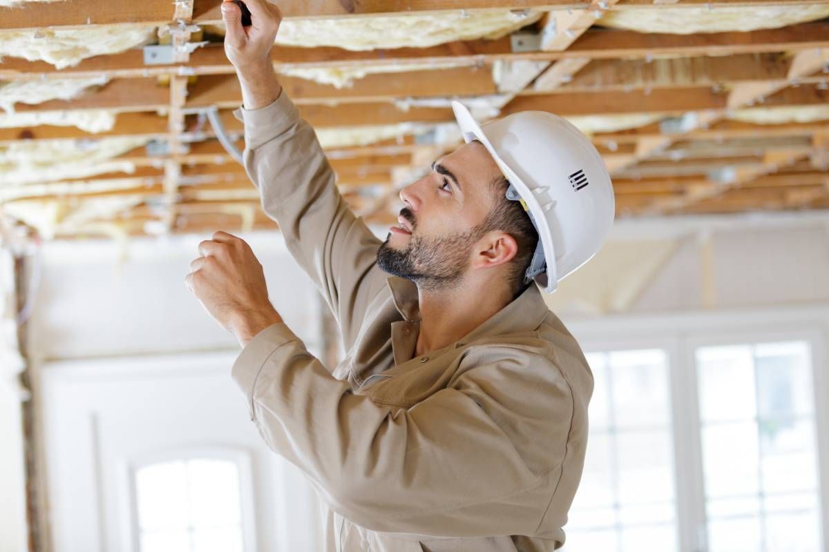 A man wearing a hard hat is working on the ceiling of a building.