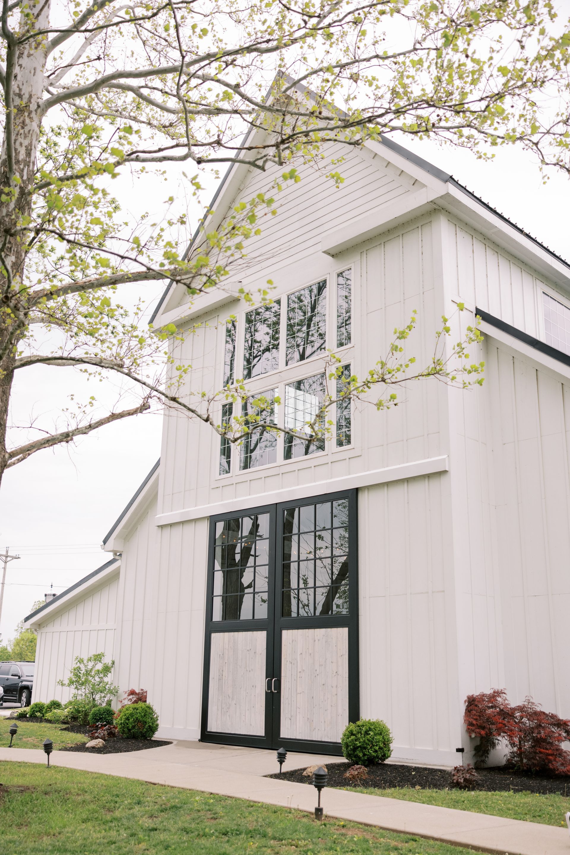 A white barn with black doors and windows is sitting on top of a lush green field.