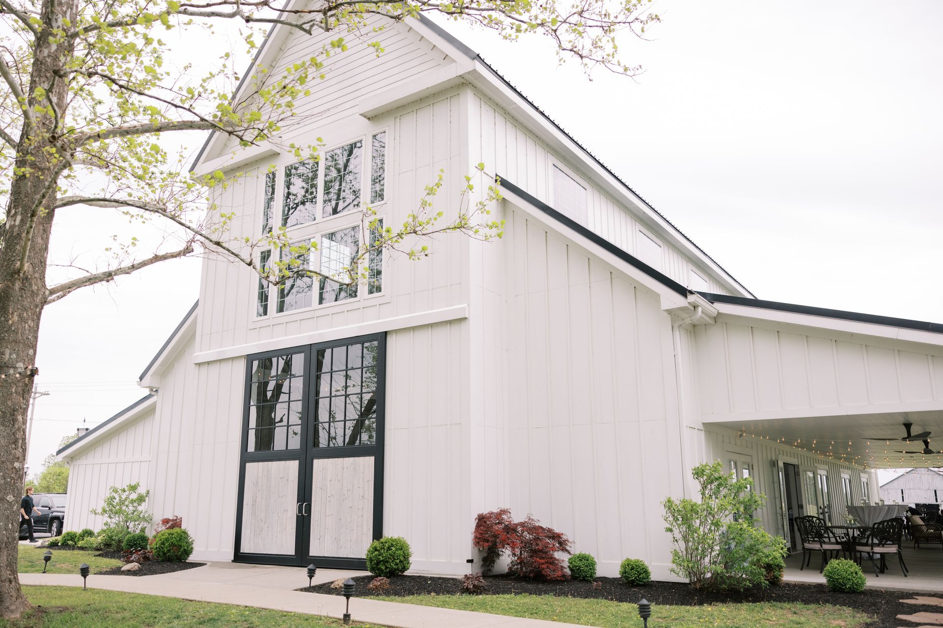 A large white barn with black doors and windows is sitting on top of a lush green field.