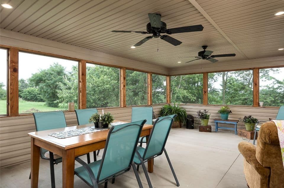 A screened in porch with a table and chairs and ceiling fans.