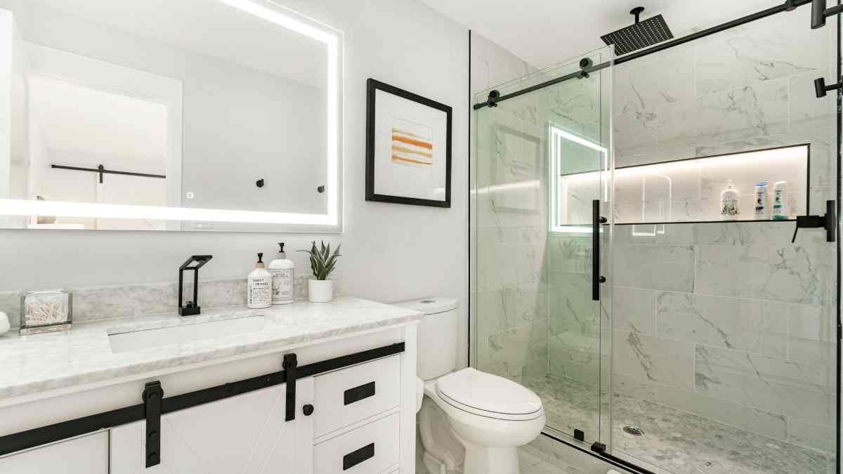 A bathroom with a toilet , sink , mirror and shower stall.