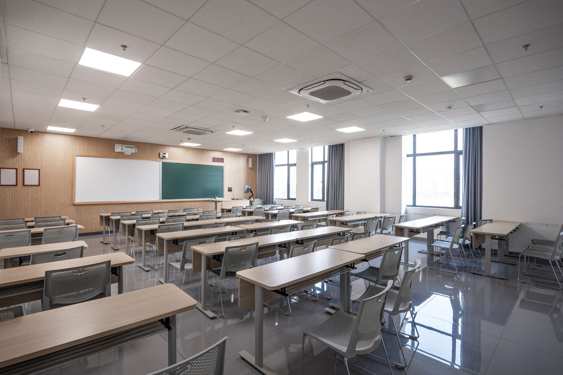 Empty classroom with rows of desks, whiteboards, and large windows.