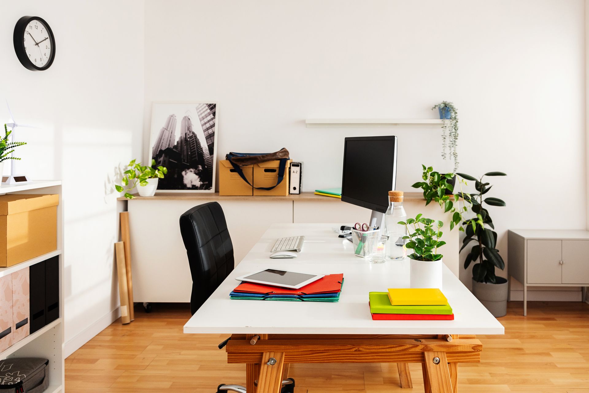 Bright, modern home office with desk, computer, plants, and art. Wooden floor and white walls.