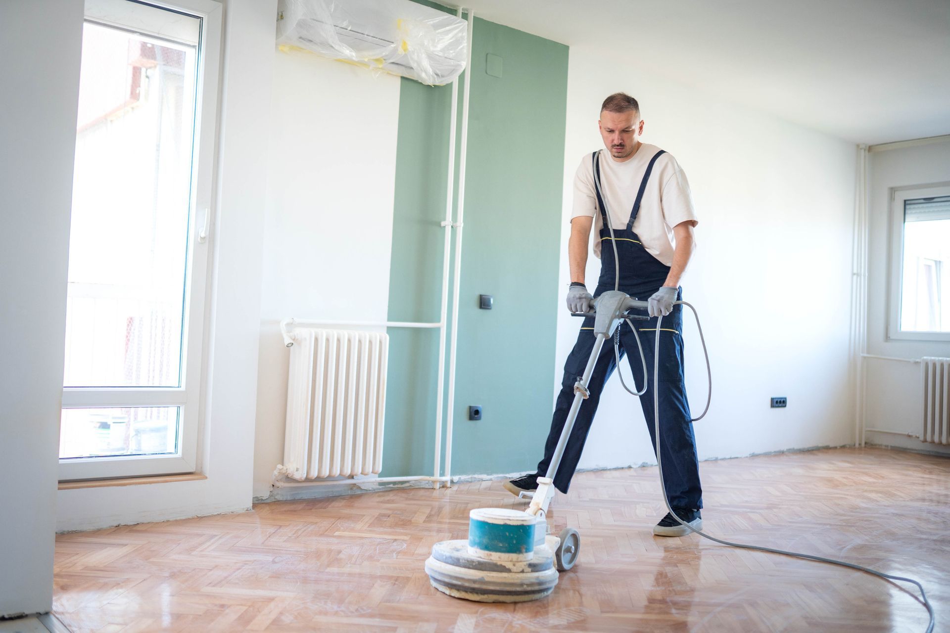 Person sanding a wooden floor in a room under renovation.