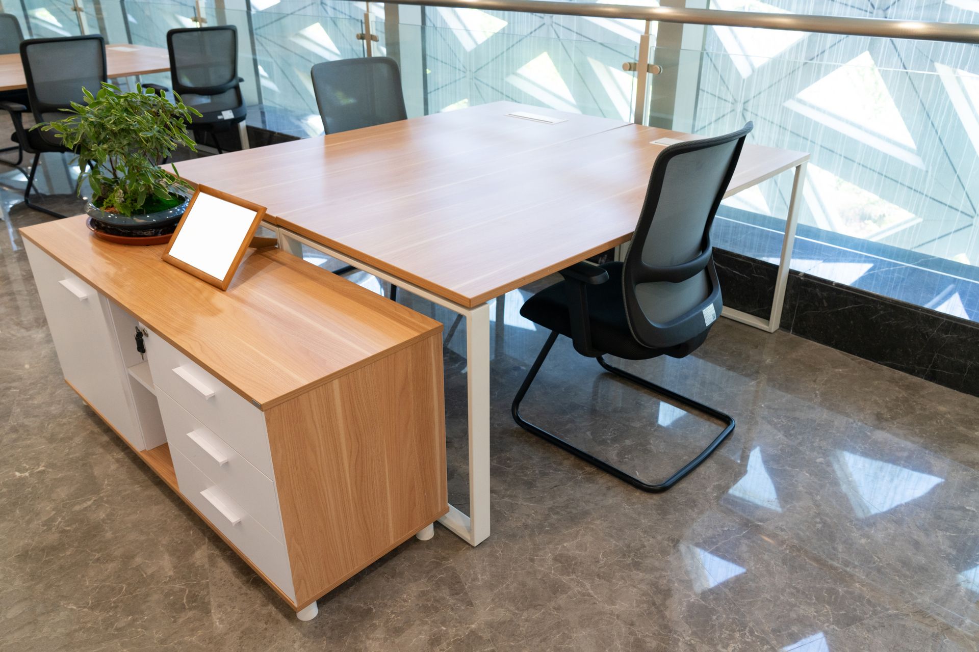 Office space with a wooden desk and chair, white and wood cabinet, and a plant.