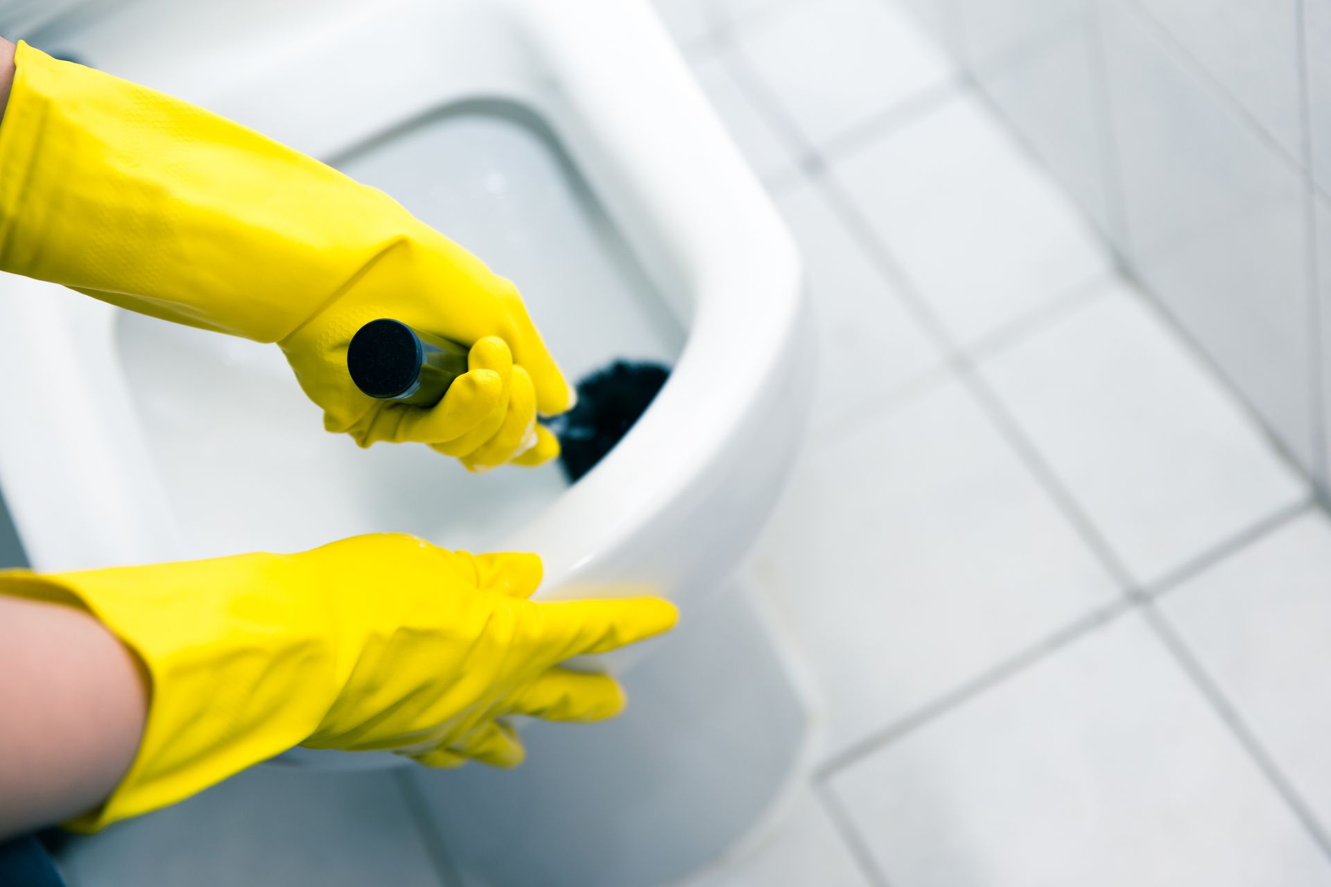 Hands in yellow gloves use a plunger in a toilet to unclog it.