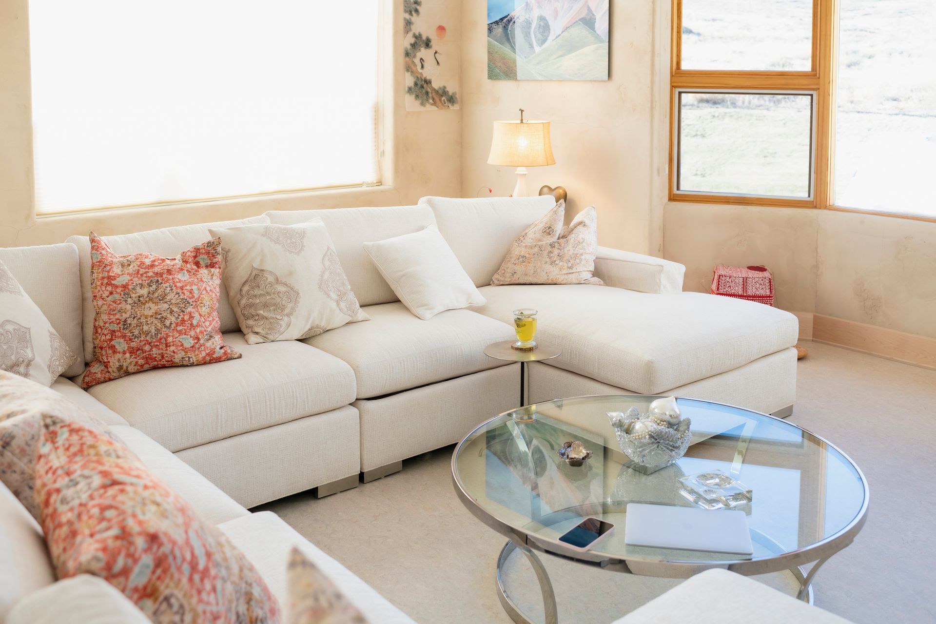 Bright living room with a white sectional sofa, round glass coffee table, and windows.