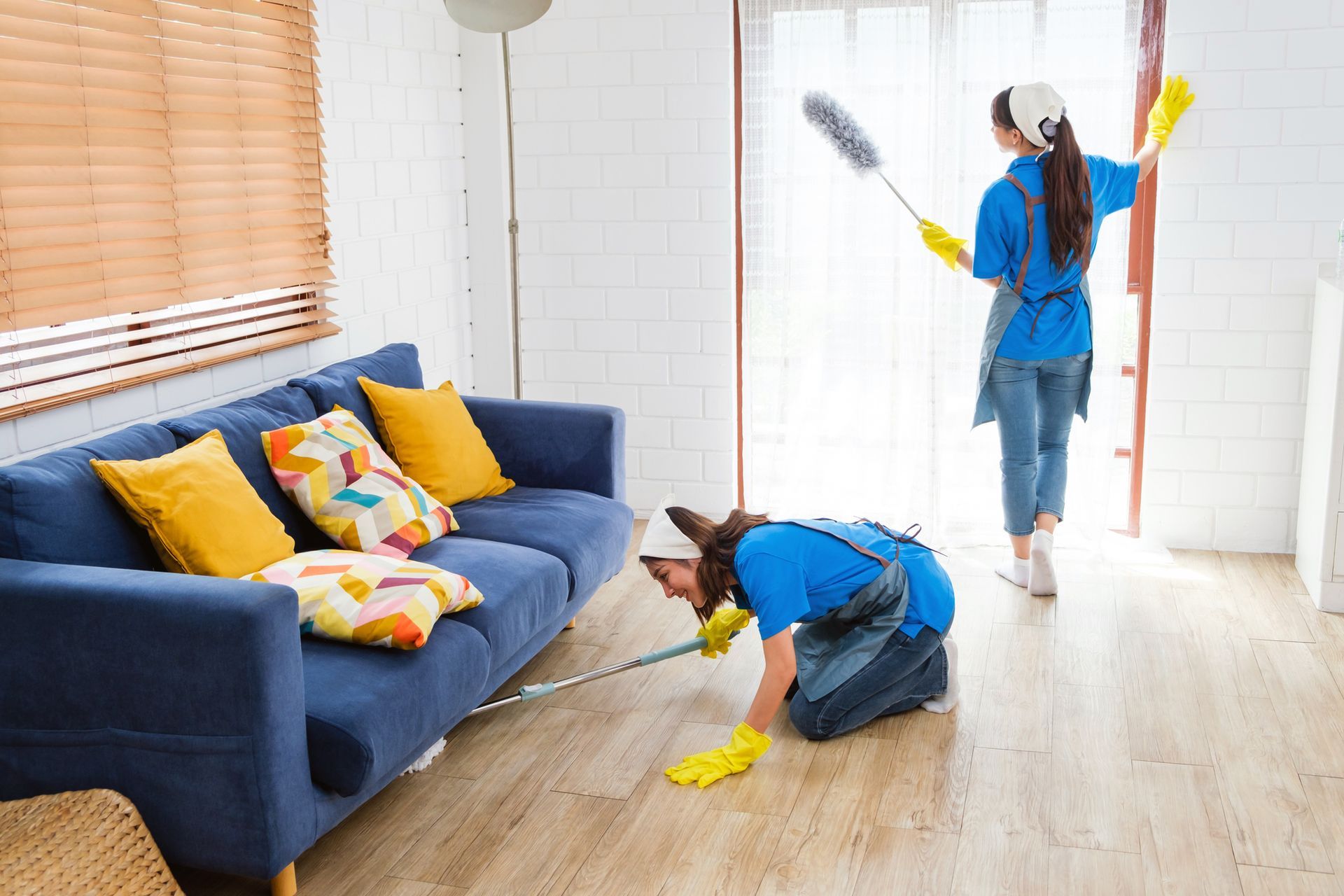 Two people cleaning a living room with a blue couch, dusting, and wiping the floor.