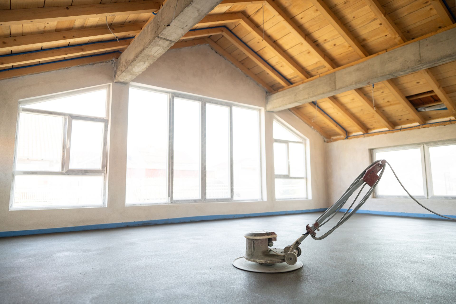 Floor sander in an unfinished room with large windows and a wooden ceiling.