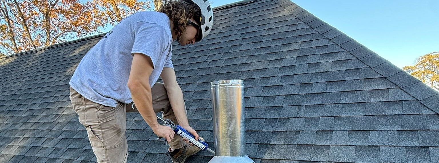 Certified chimney technician on a shingled roof, sealing around a metal vent pipe