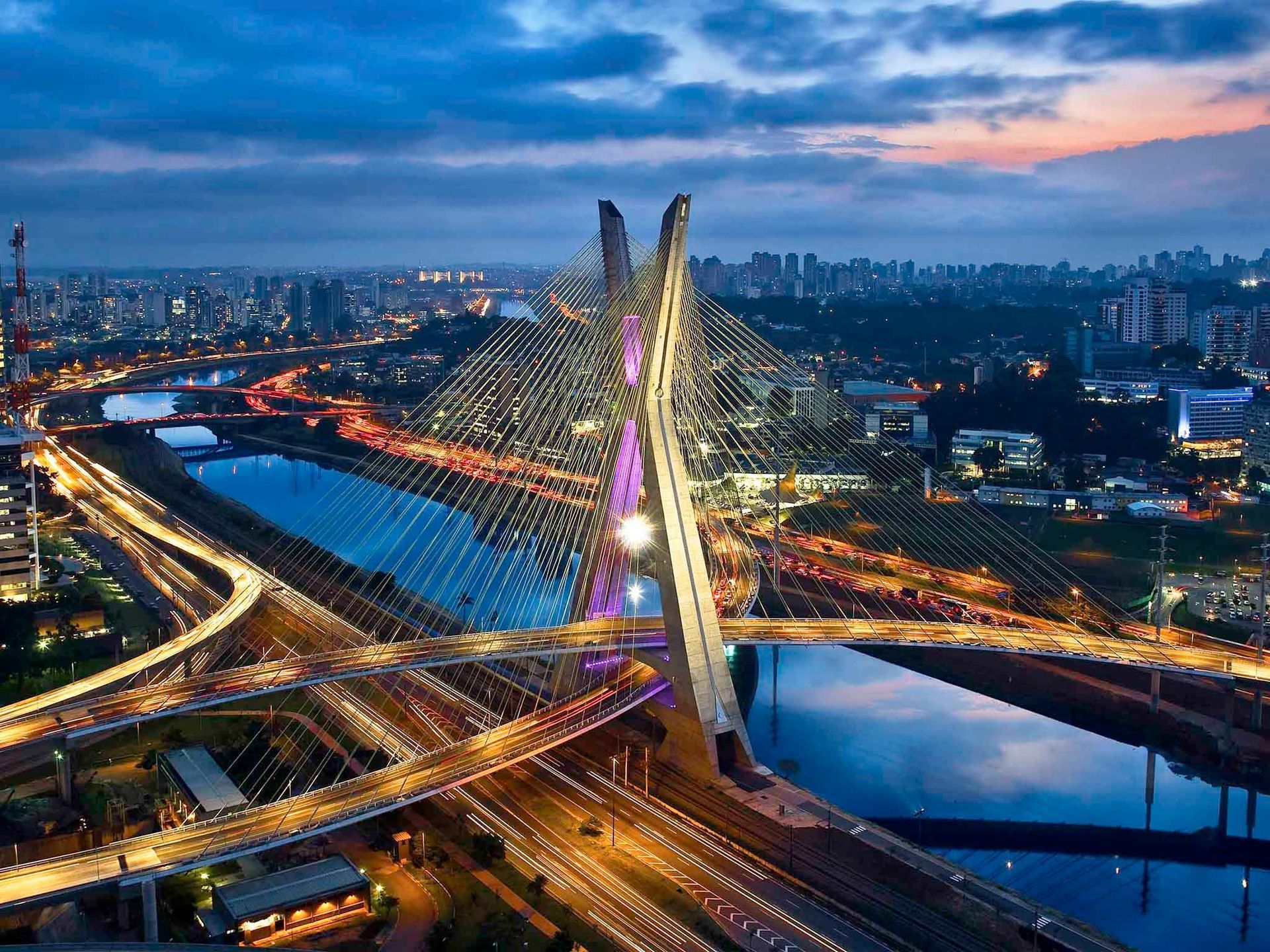 Ponte estaiada em São Paulo, Brasil, ao anoitecer; iluminada com luzes sobre um rio, com o horizonte da cidade ao fundo.