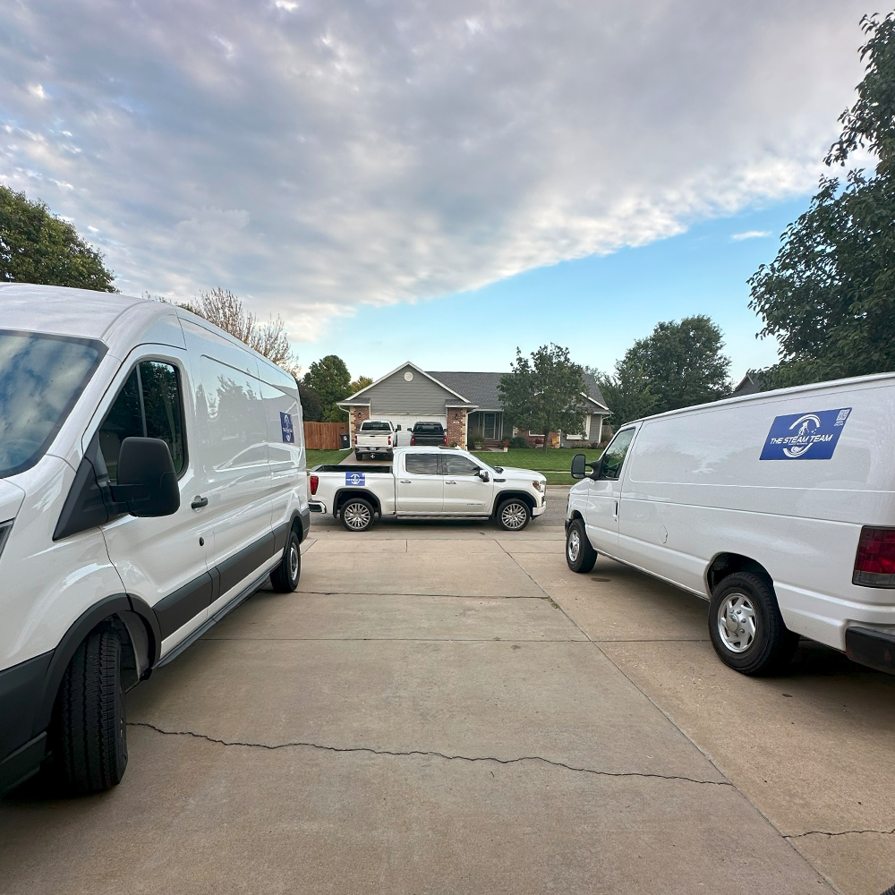 three white vans are parked in a driveway in front of a house