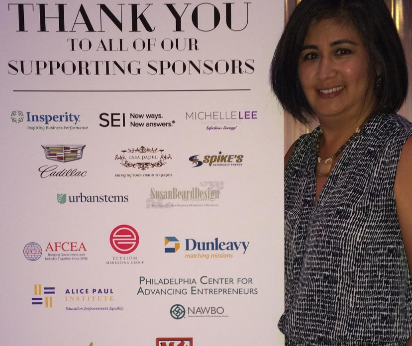 A woman stands in front of a sign that says thank you to all of our supporting sponsors
