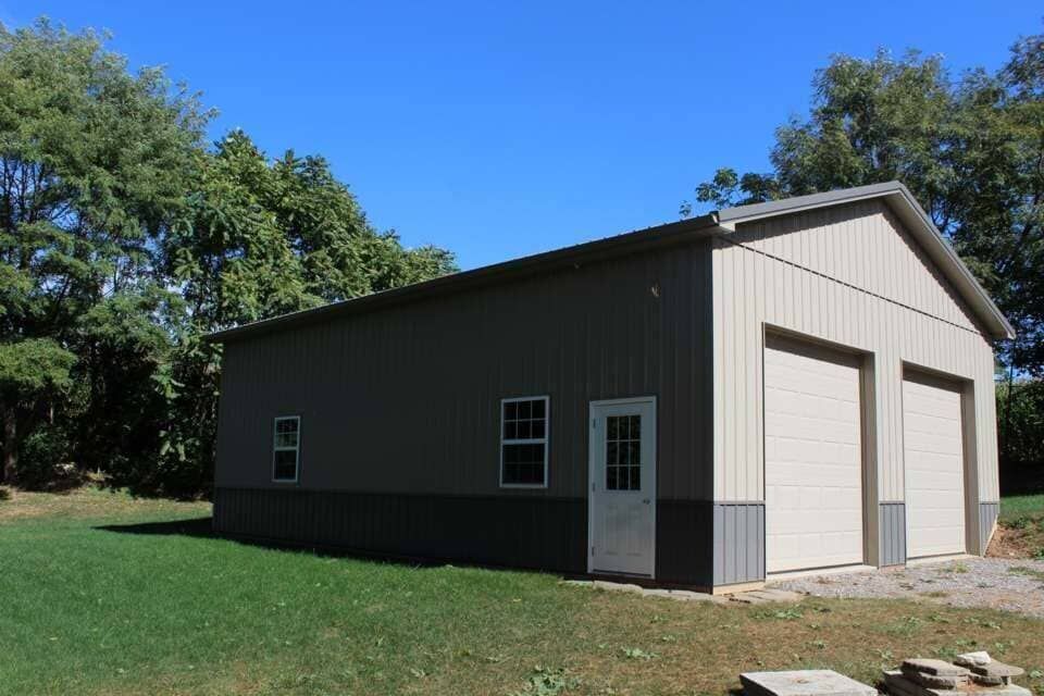 A garage with two garage doors is sitting in the middle of a grassy field.