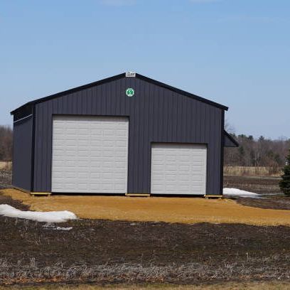 A black garage with two white garage doors is sitting in the middle of a field.