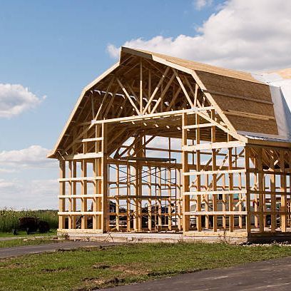 A large wooden barn is being built in a field.