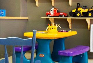 Une table et des chaises Little Tikes dans une pièce avec des jouets sur des étagères.