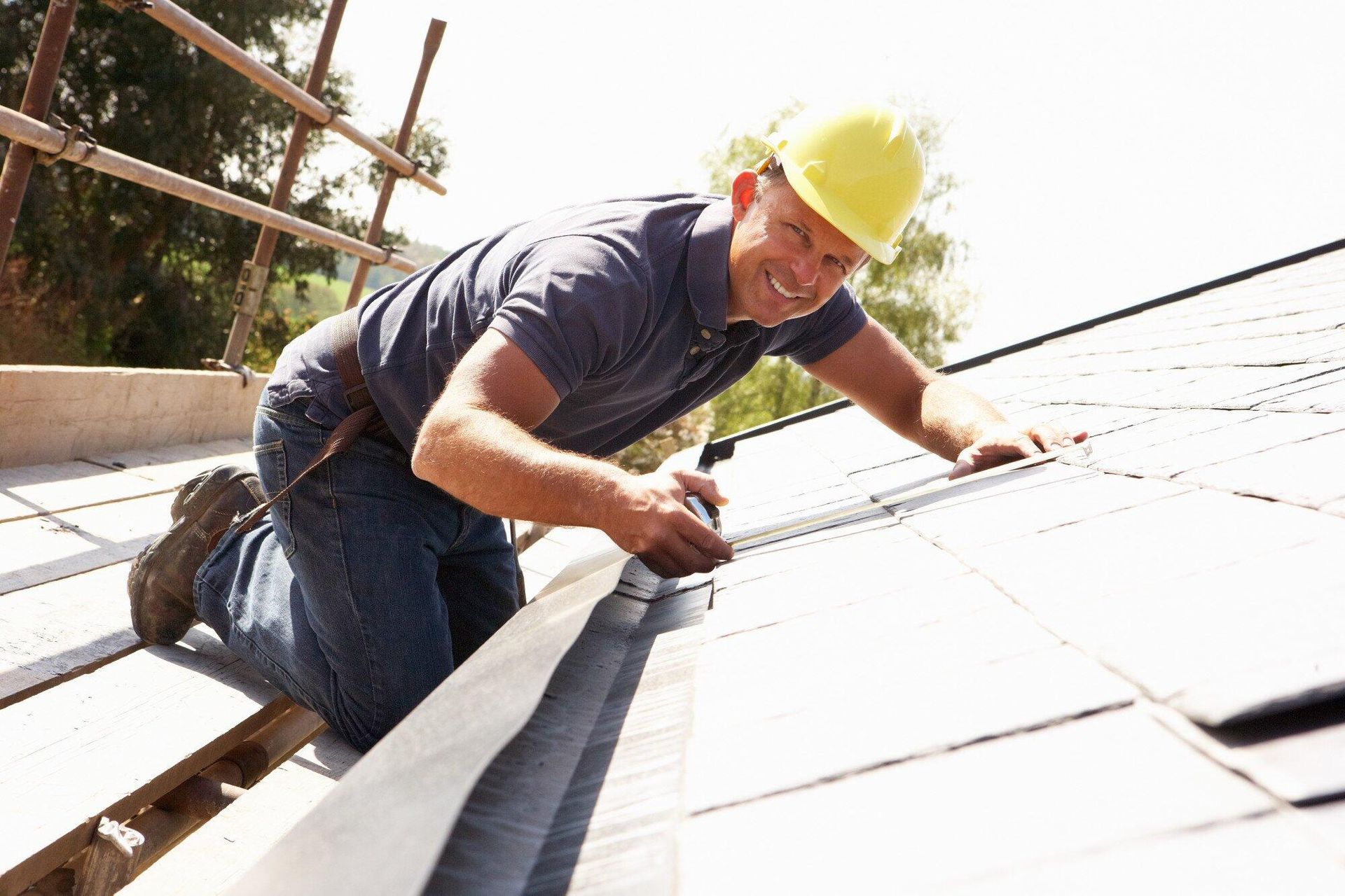 A man wearing a hard hat is working on a roof.