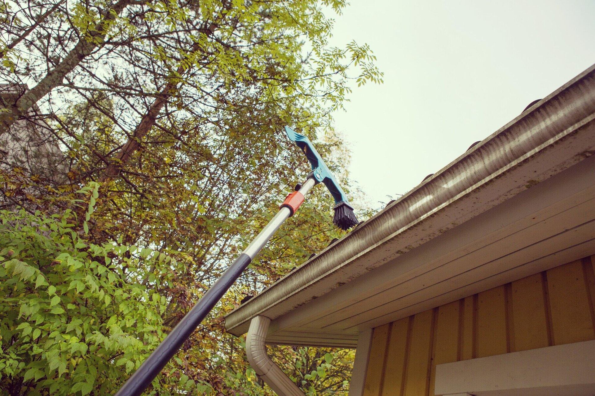 A person is cleaning the gutters of a house with a long pole.