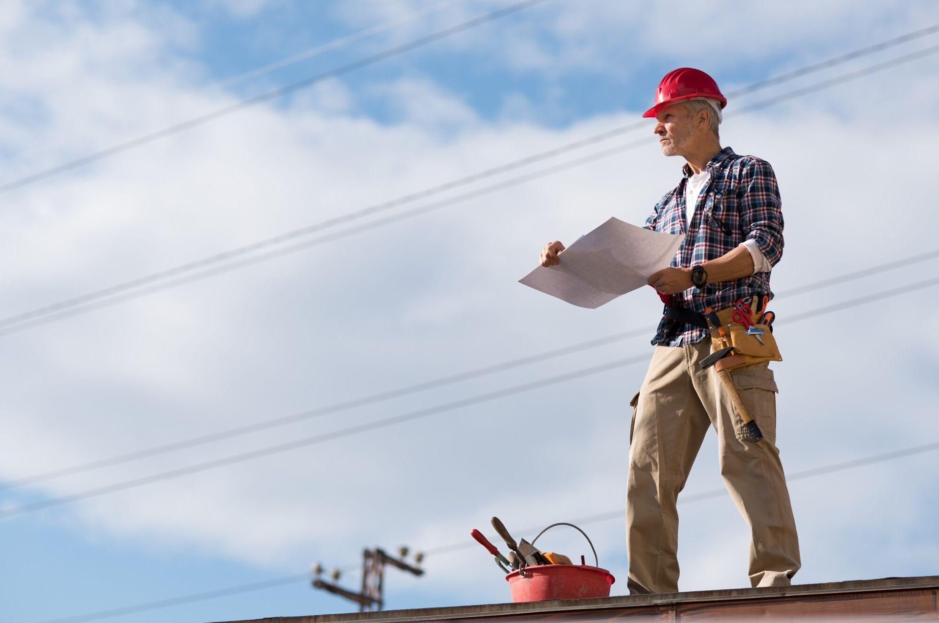 Engineer standing on rooftop looking away and holding blueprint project. Mature construction worker 