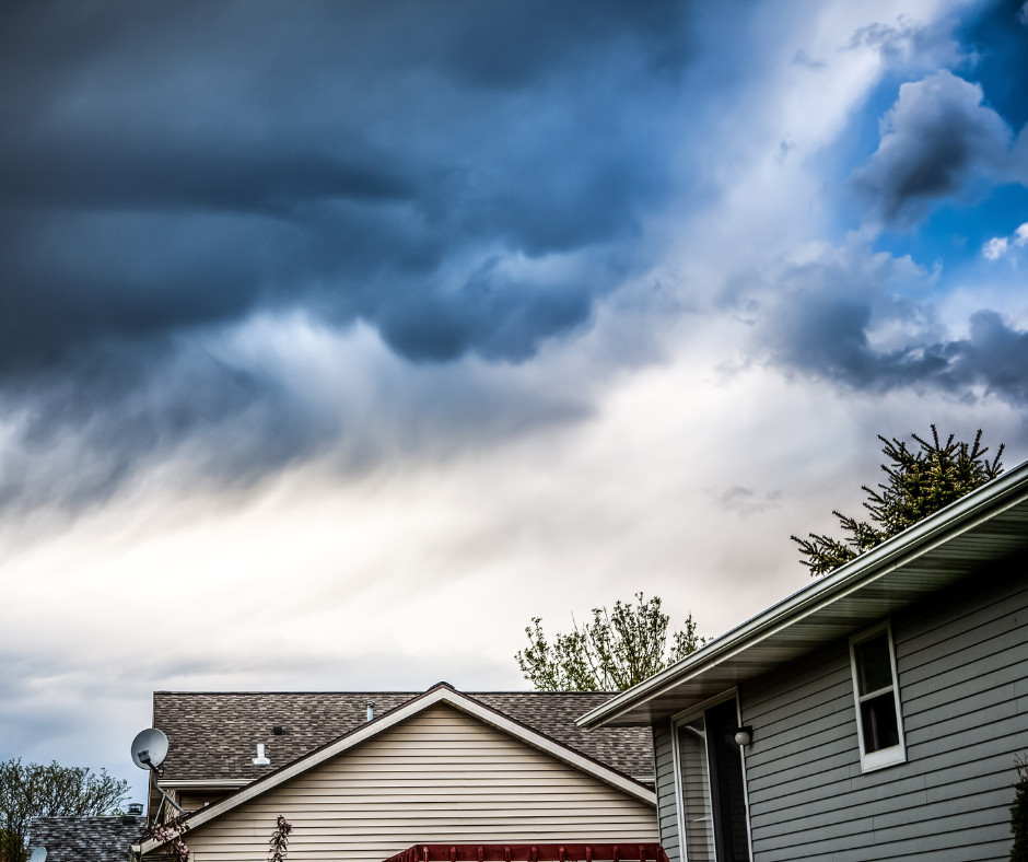 Dark stormy sky over houses; ominous clouds, gray siding, and tree tops visible.