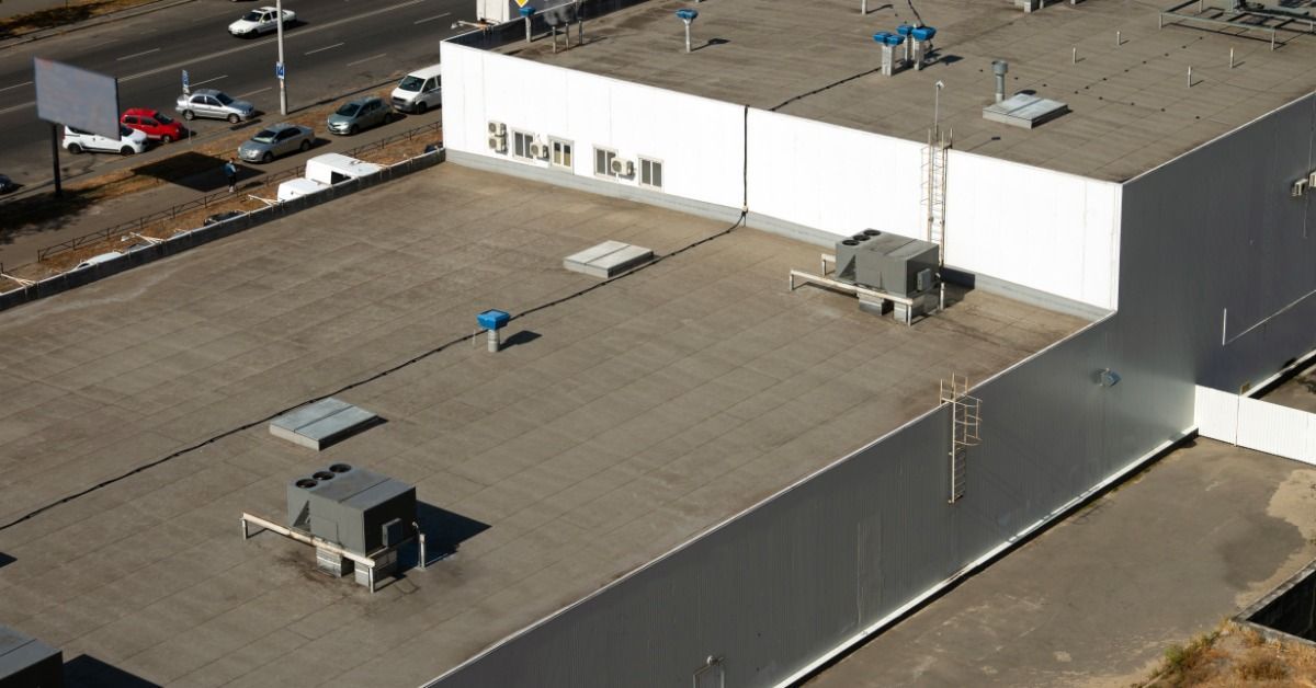 An aerial view of a large flat commercial building roof with HVAC units, vents, and skylights beside