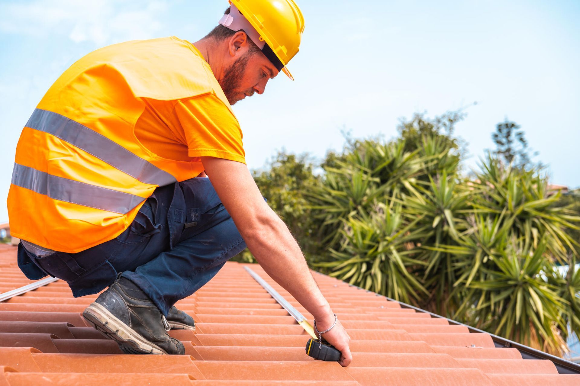 A construction worker is measuring the roof with a tape measure.