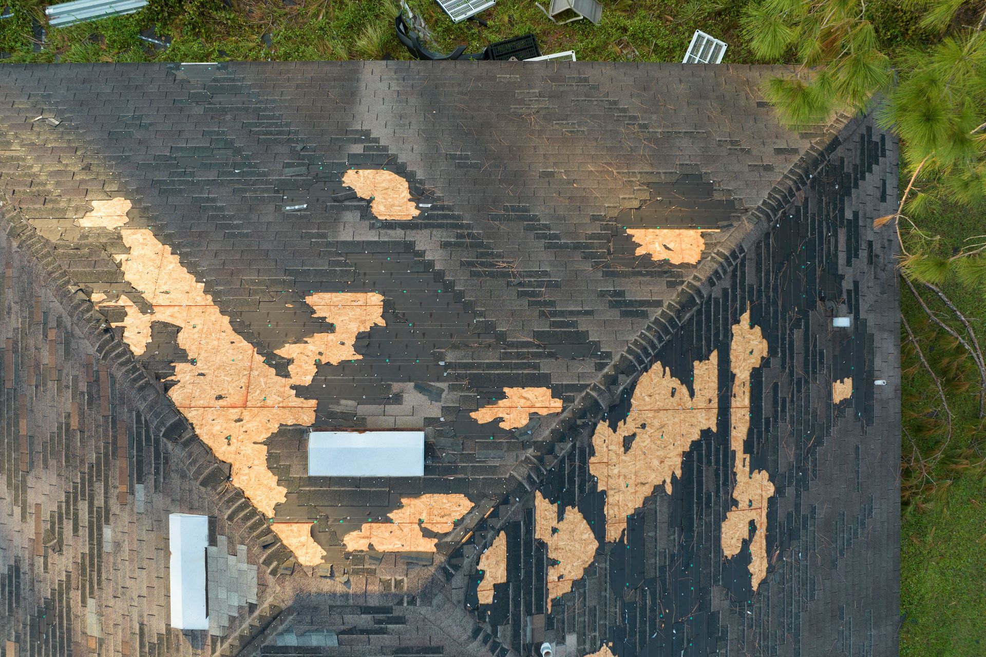 Aerial view of a damaged roof with large patches of missing shingles, showing the underlayment.