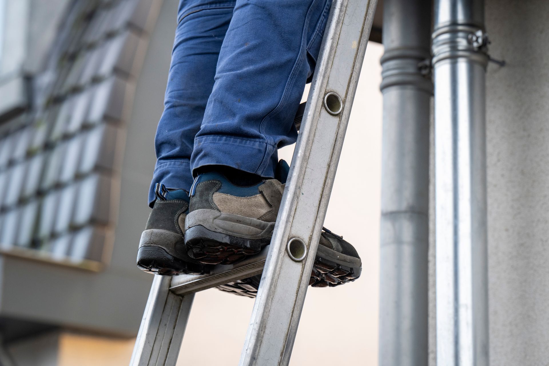 Person standing on a ladder beside metal pipes on a building exterior.