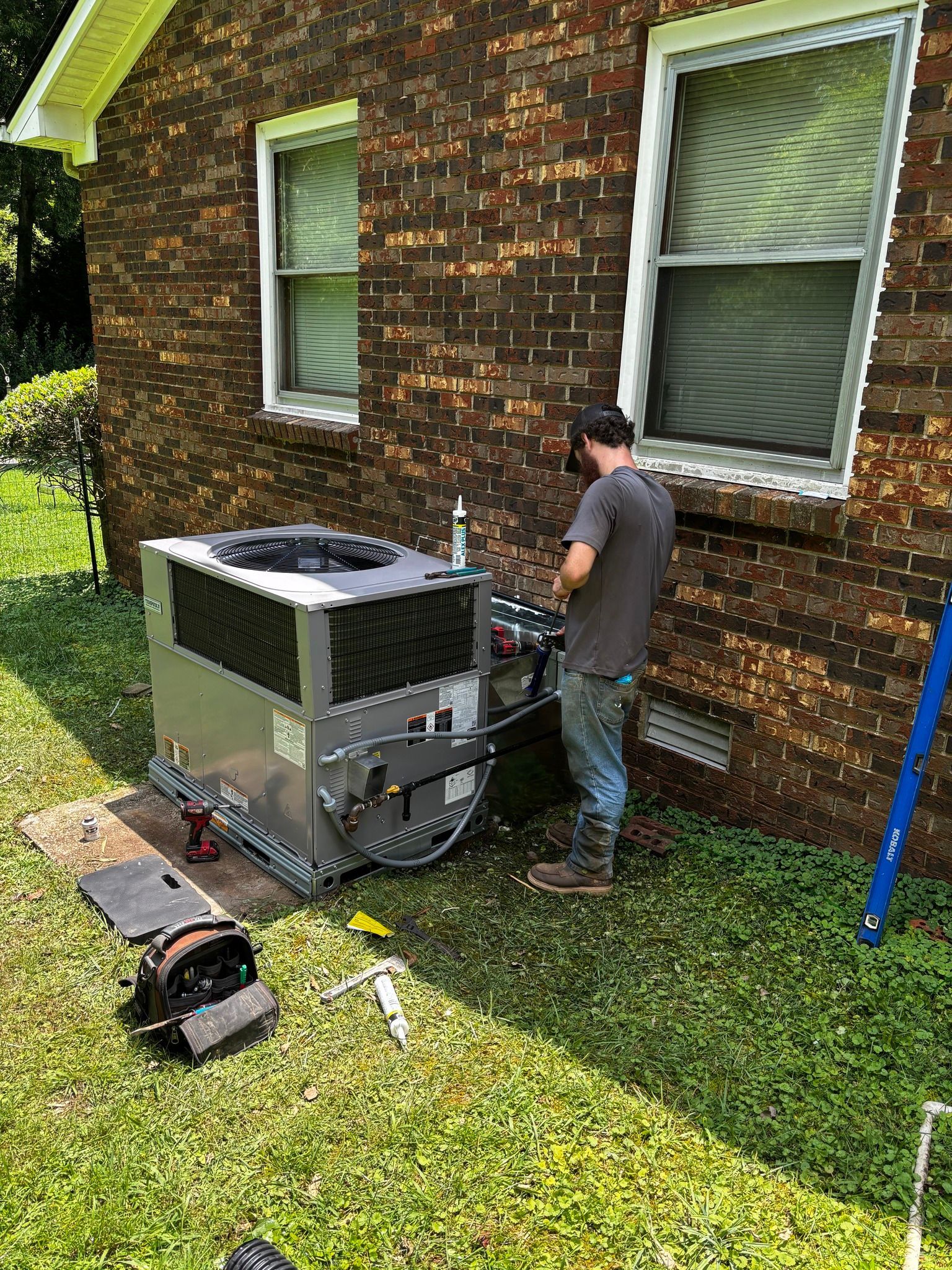 HVAC technician working on an air conditioning unit outside a brick building.
