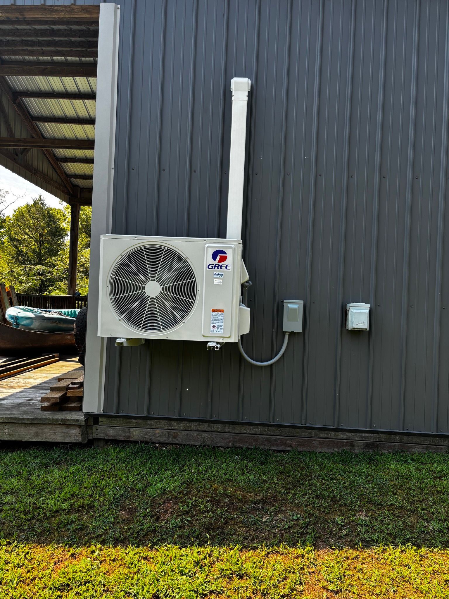 Mini-split AC unit mounted on a gray metal building exterior wall with white conduit.
