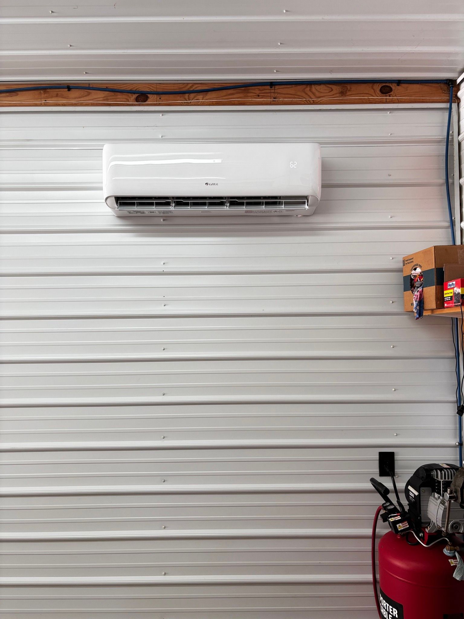 White wall-mounted air conditioner on a corrugated metal wall in a workshop.