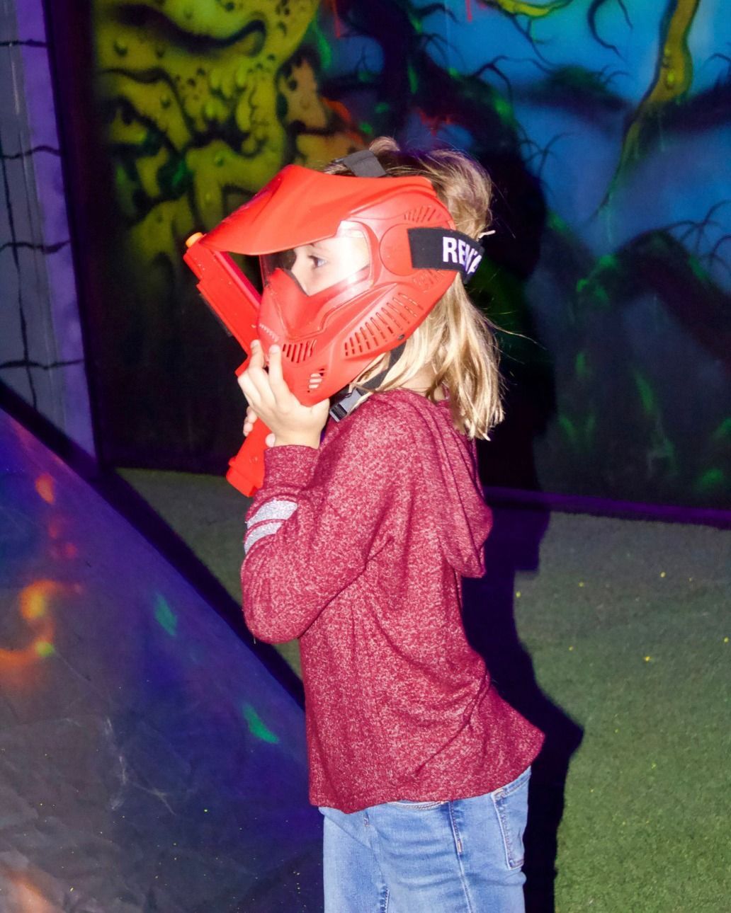 A little girl is wearing a red paintball mask