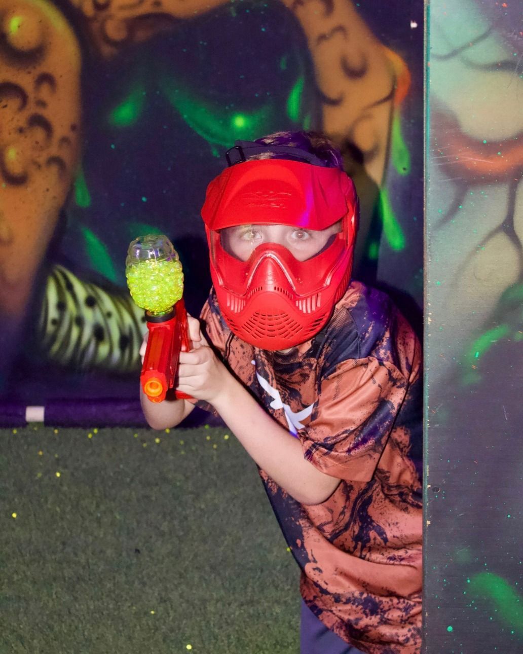 Player in a red mask aiming a toy blaster in a blacklight arena.