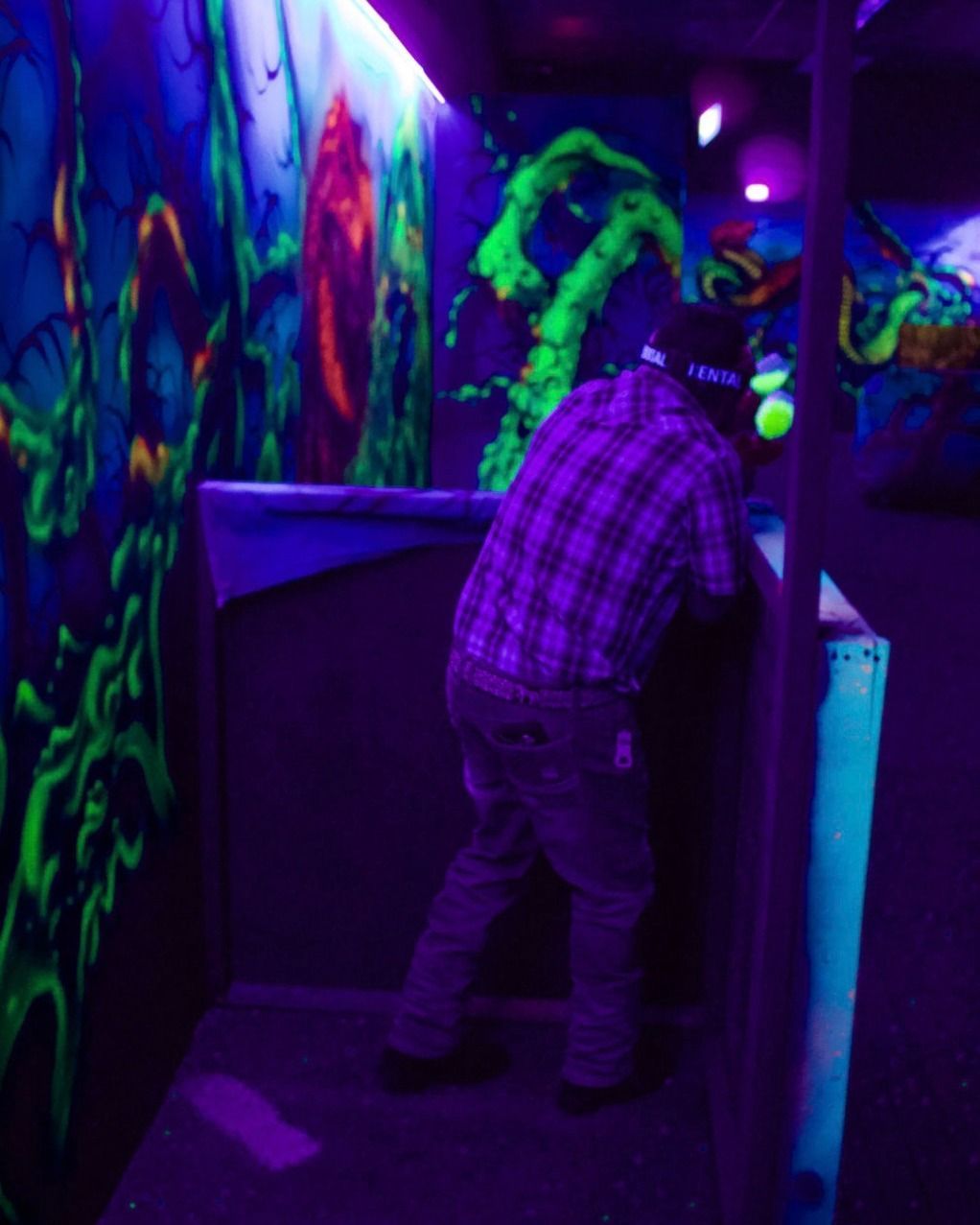 A man in a plaid shirt is standing in a dark room with glow in the dark paintings on the walls