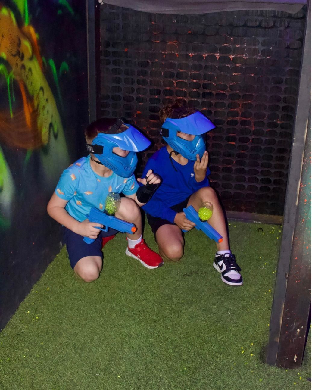 Two young boys wearing paintball masks are playing a game of paintball