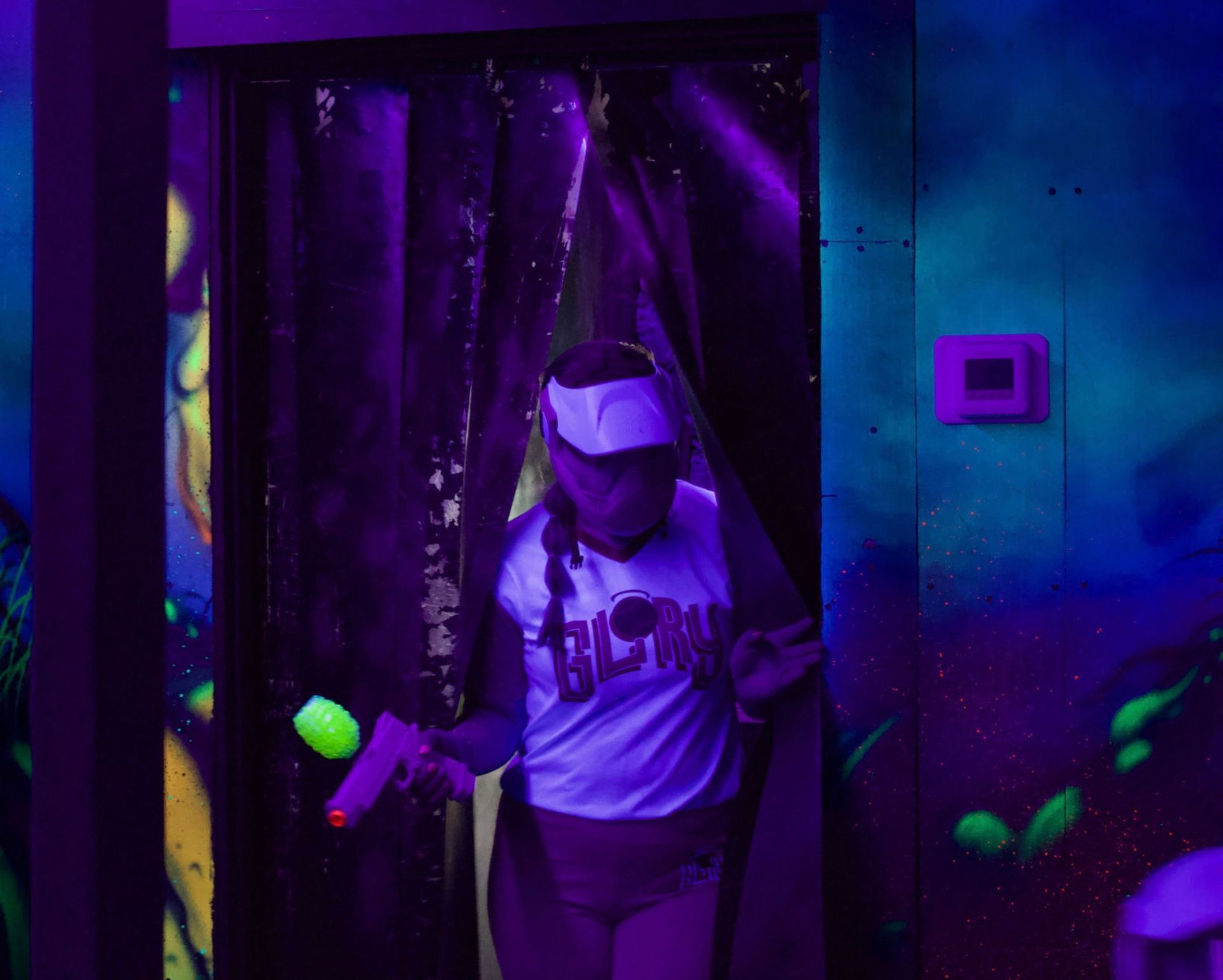 Player in a glowing visor stepping into a blacklight arena with a toy blaster.