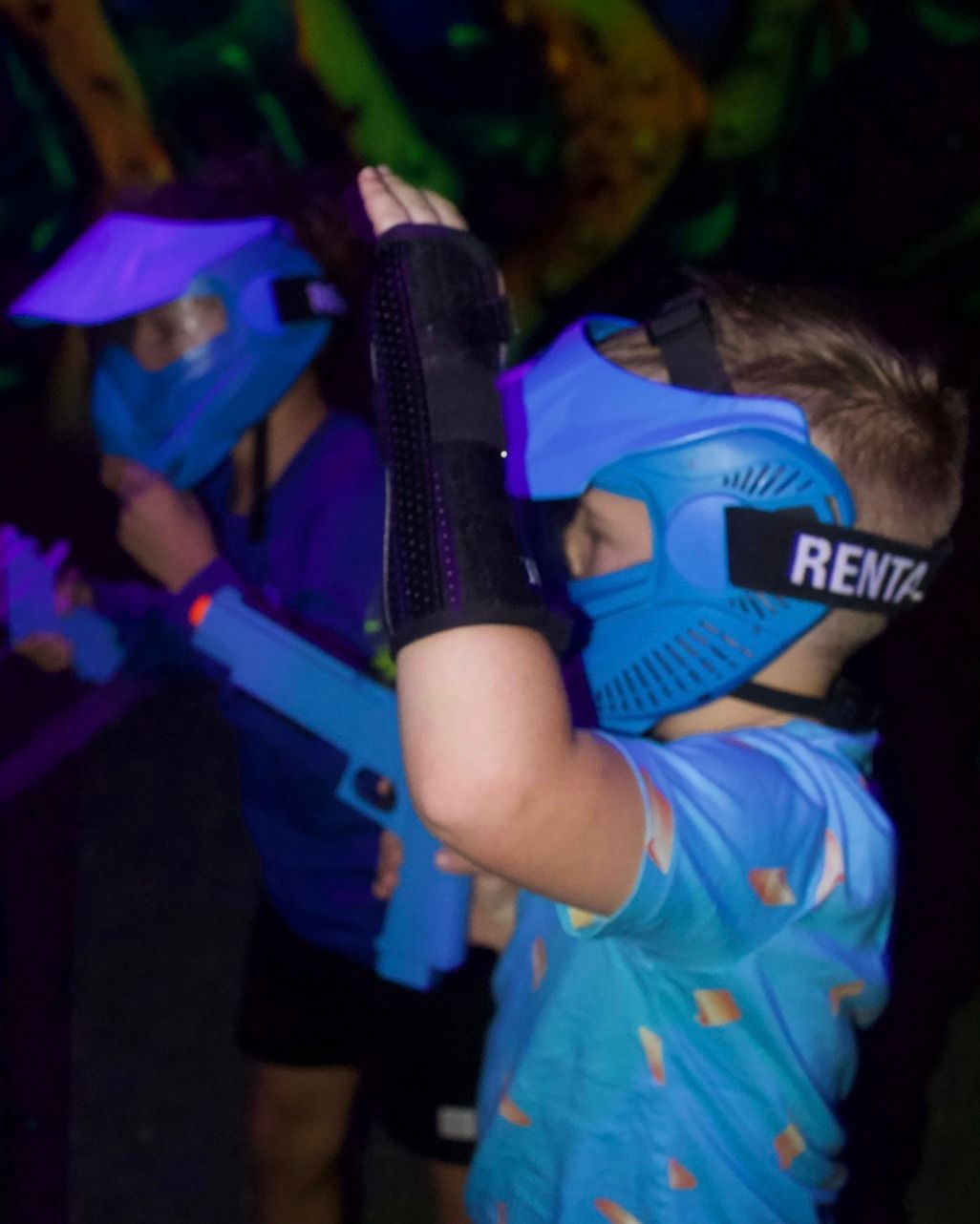 Players in blue masks aiming toy blasters in a blacklight arenaZZ