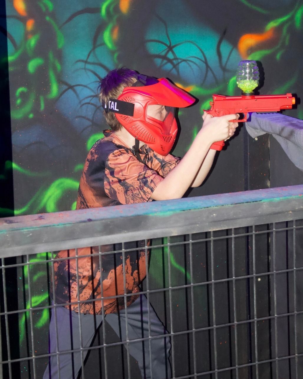 Player in a red mask aiming a toy blaster in a blacklight arena.