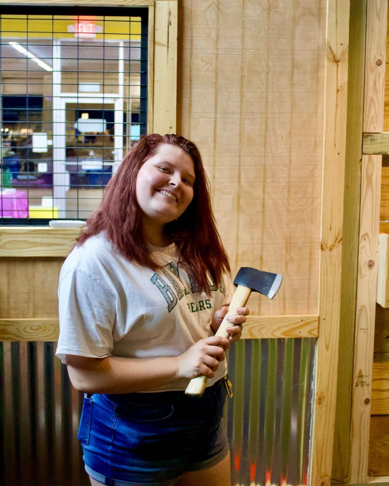 Smiling person holding an axe at an indoor axe-throwing venue.