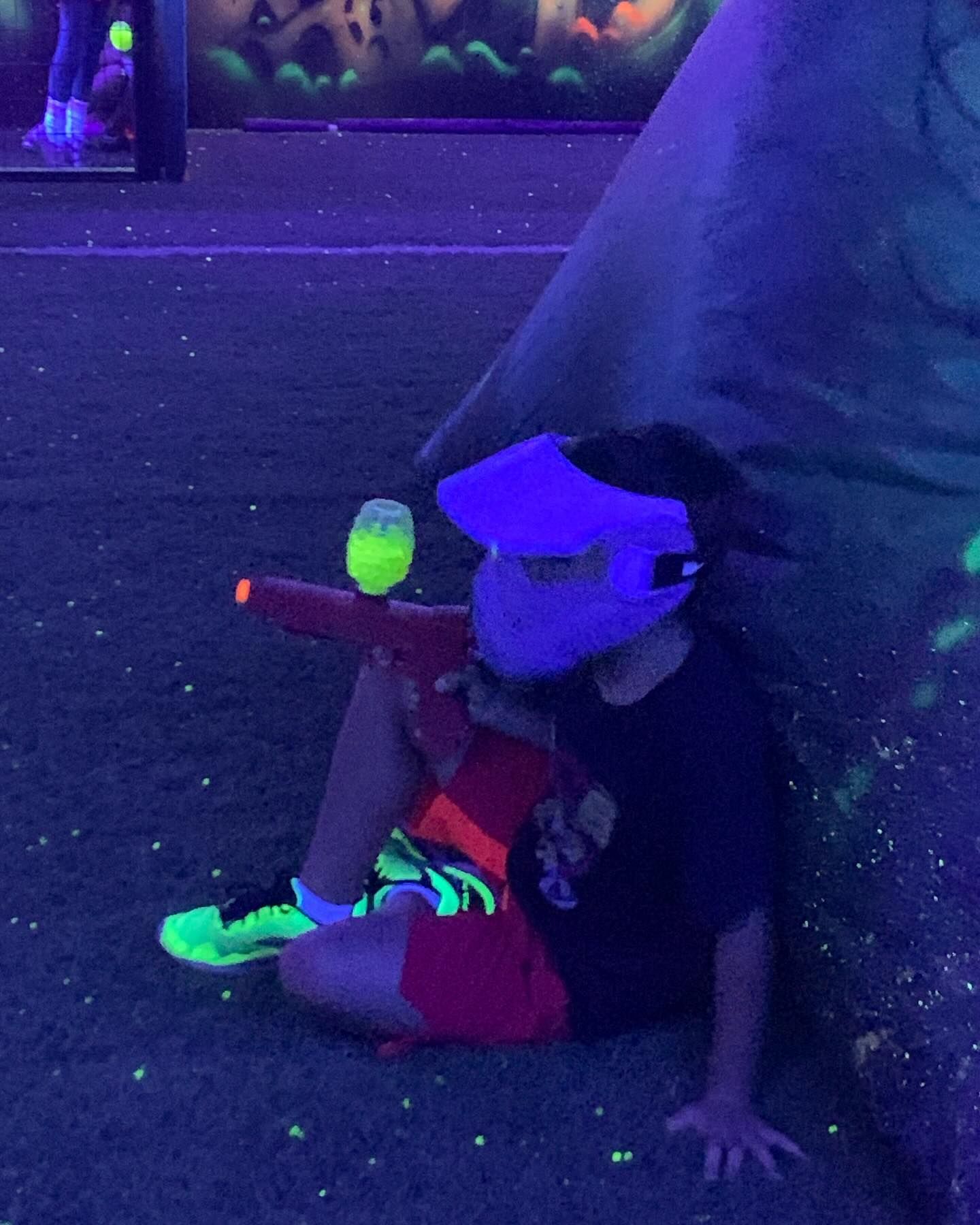 Person in a glowing visor aiming a toy blaster under blacklight.