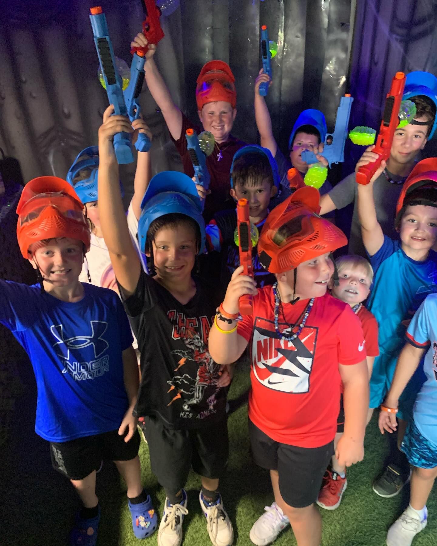 Group of kids in colorful gear holding toy blasters, smiling and cheering.