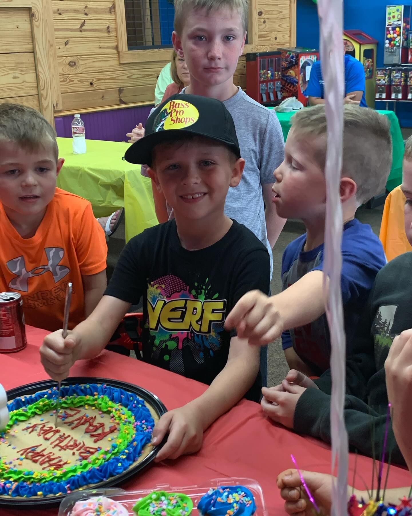 A boy wearing a shirt that says verf is cutting a birthday cake