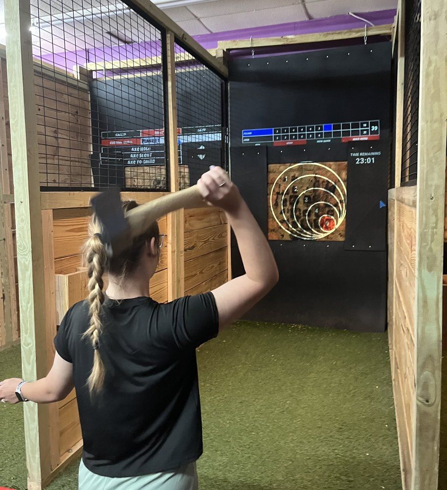 Person with a braided hairstyle throwing an axe at a target in an indoor axe-throwing range.