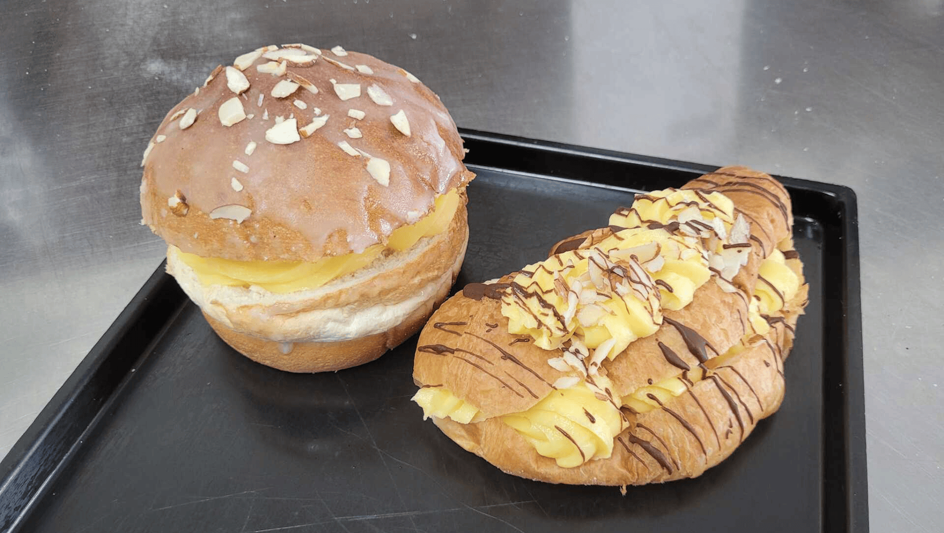 Two Pastries on a Tray a Round One Topped With Nuts and a Crescent-shaped One With Cream and Chocolate Drizzle