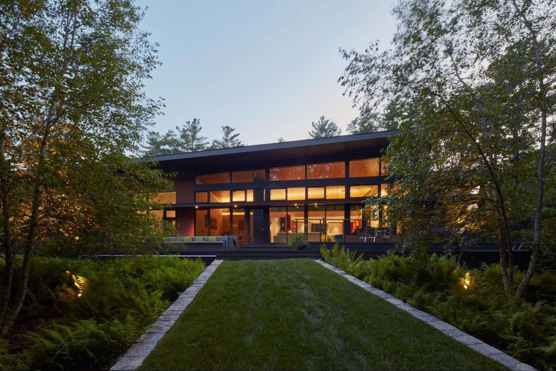 A contemporary house with lots of windows is surrounded by trees